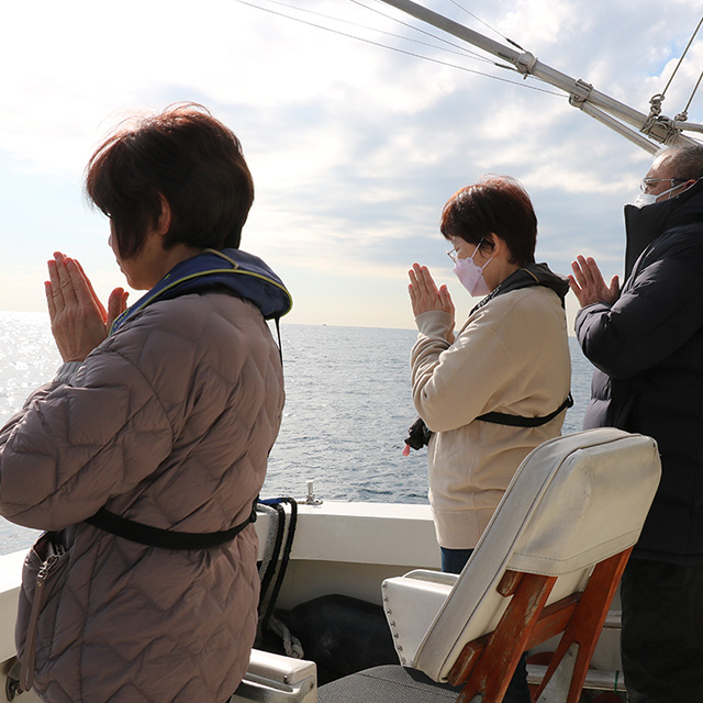 海に向かい手を合わせている女性